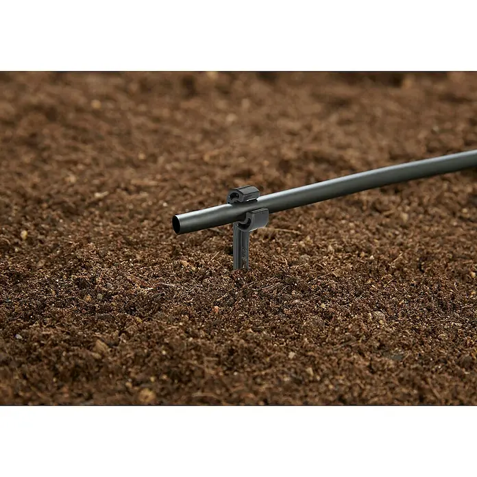 Gardena Micro-Drip Rohrhalter - 15 Stk., Größe Anschluss: ³⁄₁₆″ - Bewässerungssystem-Detail: Ein schwarzer Schlauch ist mit einer Halterung im Boden befestigt, ideal für präzise Gartenbewässerung.