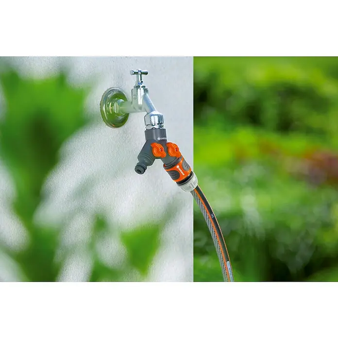 Gardena 2-Wege-Ventil - ¾″ - Gardena Wasserhahn mit Adapter für Gartenschlauch mit Sprühdüse und orangefarbenen Bedienelementen an einer weißen Wand.