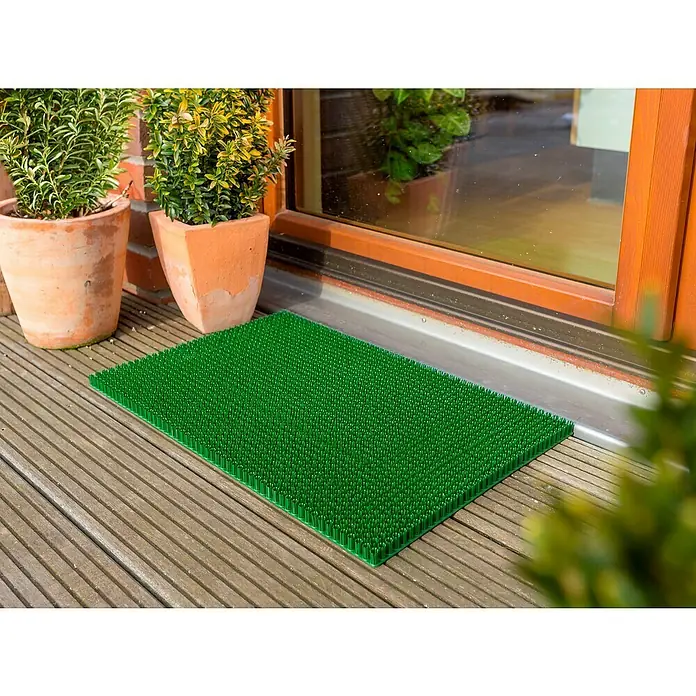 Astra Universalmatte Season - 40 x 60 cm, Grün, Material Nutzschicht: 100 % Polyethylen - Eine grüne Fußmatte mit Noppen liegt vor einer Haustür mit Pflanzenkübeln daneben. Die Matte ist rechteckig und aus Kunststoff.