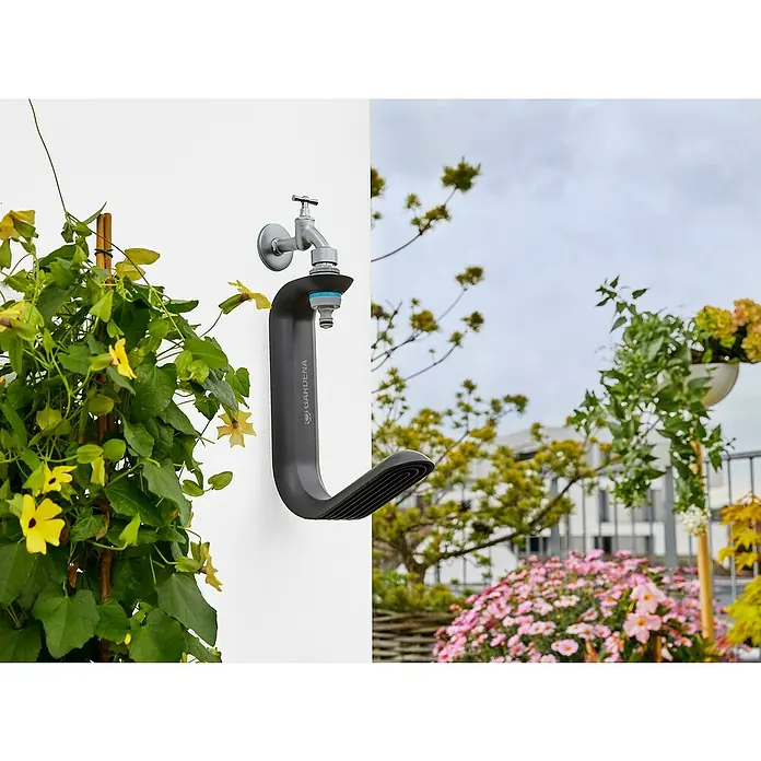 Gardena Wand-Schlauchhalterung TapFix - Passend für: Gardena Textilschlauch Liano bis 20 m, Kunststoff - Ein Gardena Wasserhahn mit Schlauchhalterung an einer weißen Wand, umgeben von üppigem Grün und Blumen.