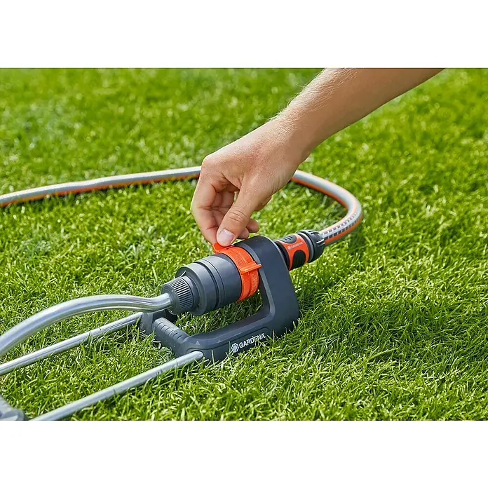 Gardena Aspersor oscilante Aqua S - Superficie de rociador máx.: 220 m² - Primer plano de un aspersor GARDENA en el césped, ajustado por una mano. Perfecto para regar tu jardín.