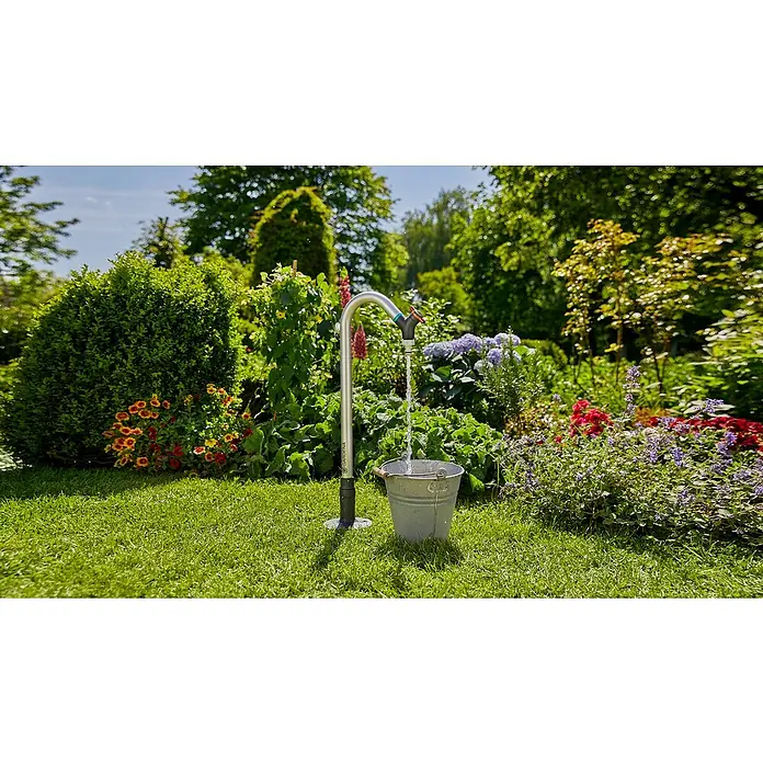 Gardena Sprinklersystem Wasserhahn - Metall - Gartenszene mit einem Gardena Wasserhahn, der Wasser in einen Metalleimer leitet, umgeben von üppiger Vegetation und Blumen.