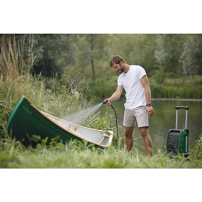 Bosch Power for All 18V Akku-Hochdruckreiniger Fontus - 18 V, Ohne Akku, Max. Druck: 20 bar - Mann reinigt ein grünes Boot mit einem Bosch-Hochdruckreiniger im Freien, mit Bäumen und Wasser im Hintergrund.