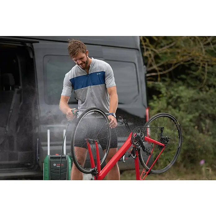 Bosch Power for All 18V Akku-Hochdruckreiniger Fontus - 18 V, Ohne Akku, Max. Druck: 20 bar - Mann reinigt ein rotes Fahrrad mit einem Bosch Hochdruckreiniger vor einem schwarzen Lieferwagen, während Sprühnebel die Luft erfüllt.