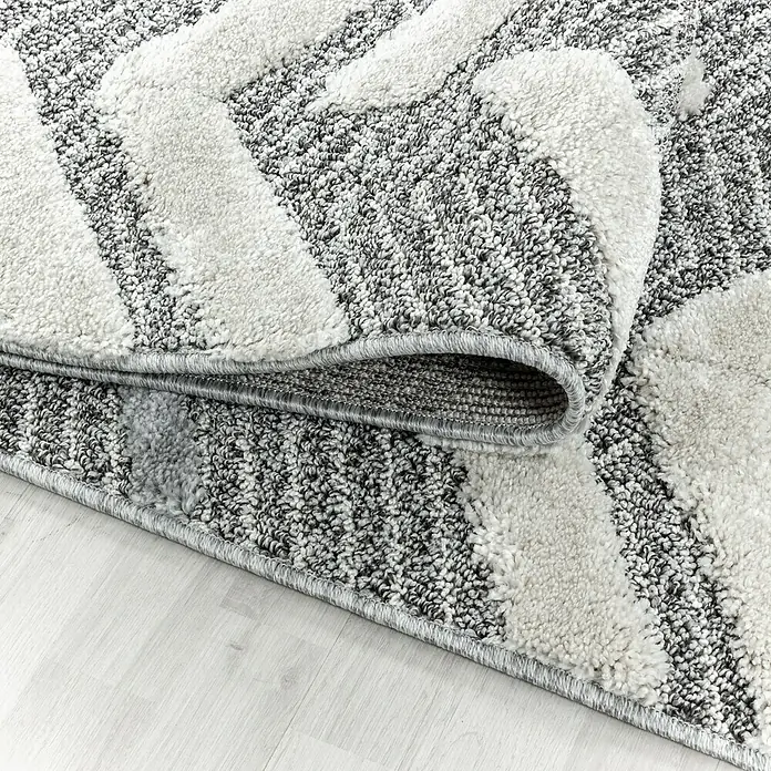 Hochflorteppich Pisa 4705Grau, 250 x 80 cm, 100% Polypropylen - Nahaufnahme eines gewebten Teppichs mit grauem Zickzackmuster und einer umgeschlagenen Ecke, der dessen Rückseite zeigt.