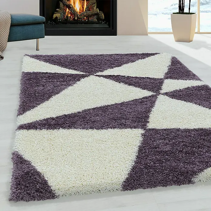 Hochflorteppich Tango 3101 - Lila, 370 x 280 cm, 100% Polypropylen - Nahaufnahme eines geometrischen Teppichs mit lila und weißen Dreiecken in einem gemütlichen Wohnzimmer.