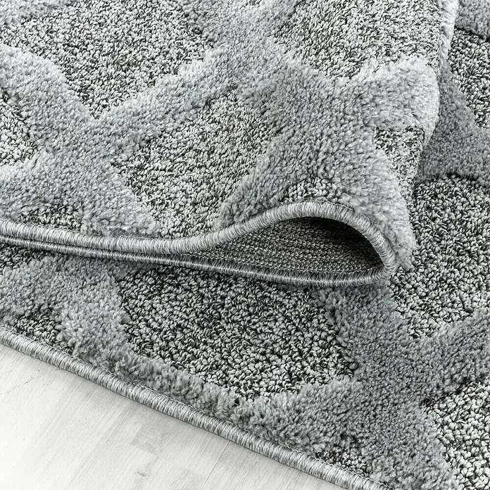 Hochflorteppich Pisa 4702 - Grau, 150 x 80 cm, 100% Polypropylen - Nahaufnahme eines grauen Teppichs mit geometrischen Mustern und gewebter Bordüre, der auf einem hellen Holzboden liegt.