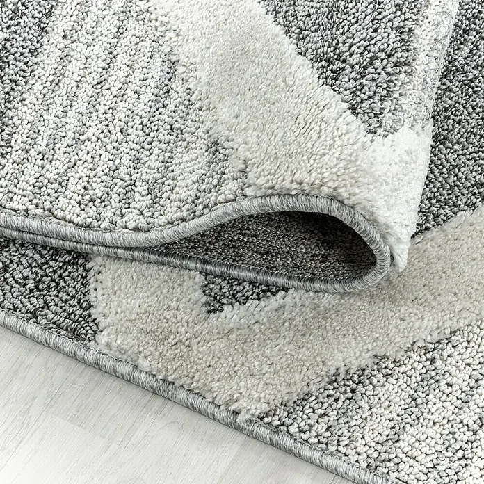 Hochflorteppich Pisa 4709 - Grau, 290 x 200 cm, 100% Polypropylen - Detailaufnahme eines modernen Teppichs in Grau- und Weißtönen mit einem gefalteten Rand, der die Textur hervorhebt.