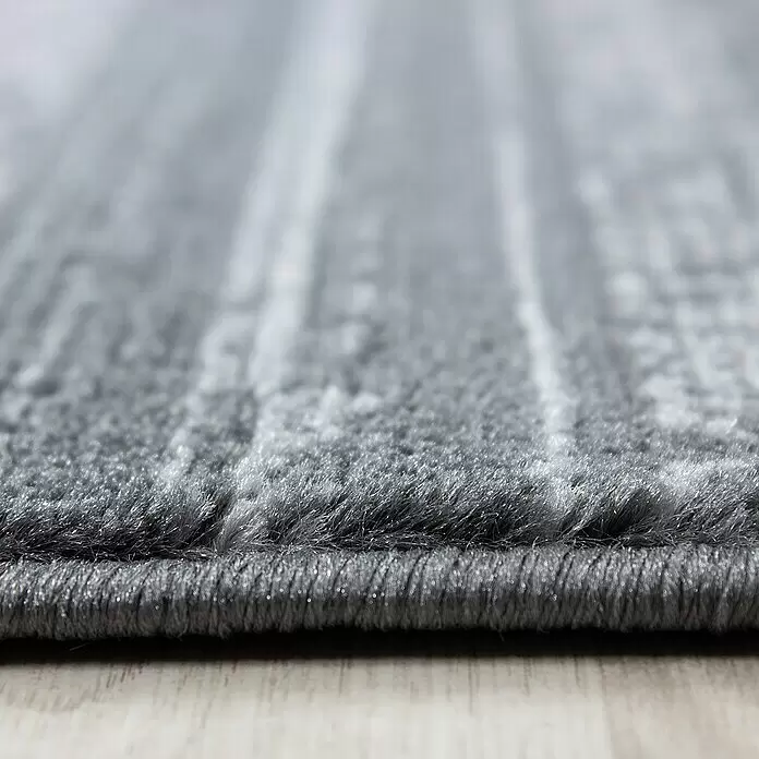 Kurzflorteppich Plus 8000 - Grau, 290 x 200 cm, 100% Polypropylen - Nahaufnahme eines grauen, strukturierten Teppichs mit weichem, flauschigem Flor, der seine gewebte Kante zeigt.