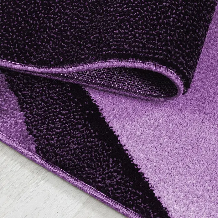 Kurzflorteppich Plus 8010 - Lila, 200 x 140 cm, 100 % Polypropylen - Nahaufnahme eines violetten Teppichs mit dunklen und hellen Farbtönen und einer abgerundeten Kante.
