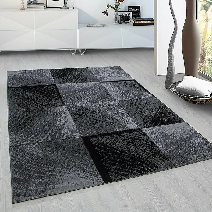 Kurzflorteppich Plus - Schwarz/Anthrazit, 370 x 280 cm, 100 % Polypropylen - Ein moderner grauer Teppich mit einem geometrischen Muster liegt auf einem hellen Holzboden in einem stilvollen Wohnzimmer.
