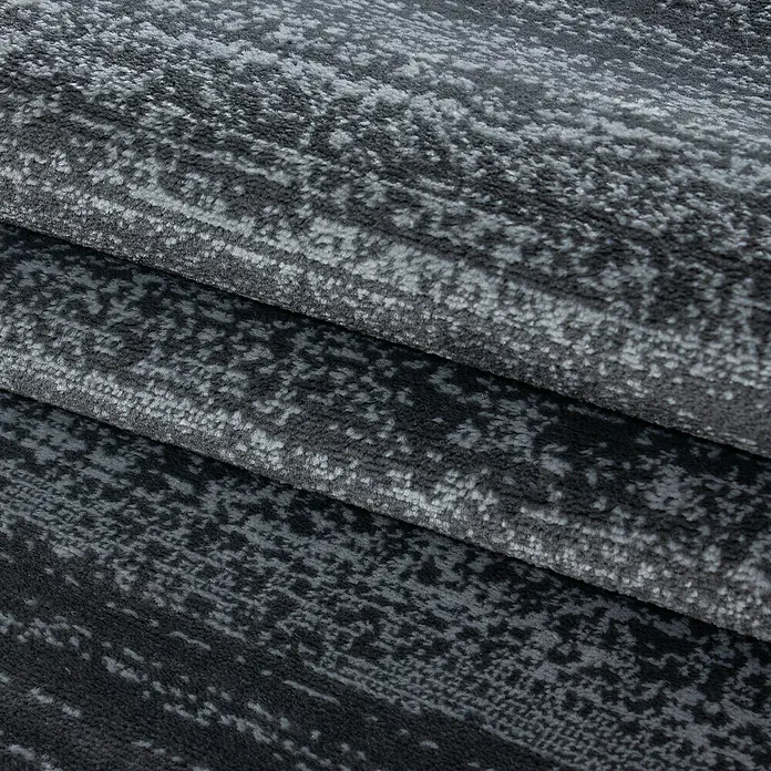 Kurzflorteppich Plus 8000 - Grau, 290 x 200 cm, 100% Polypropylen - Nahaufnahme eines gefalteten, dunkelgrauen Teppichs mit abstraktem Muster, der Textur und Tiefe zeigt.\n