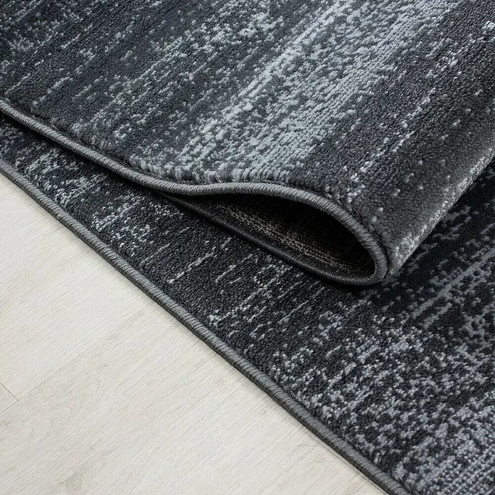 Kurzflorteppich Plus 8000 - Grau, 290 x 200 cm, 100% Polypropylen - Detailaufnahme eines modernen grauen Teppichs mit abstraktem Muster und umgeschlagener Ecke.