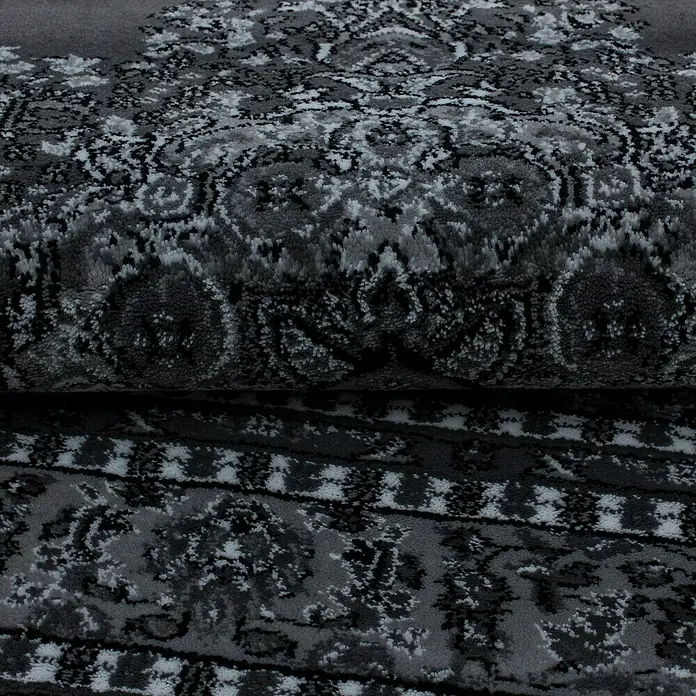 Kurzflorteppich Orient-Optik Marrakesh 0297 - Grau, 150 x 80 cm, 100% Polypropylen - Nahaufnahme eines grauen Teppichs mit kompliziertem, dunklem Muster, gerollt, der eine elegante und strukturierte Oberfläche zeigt.