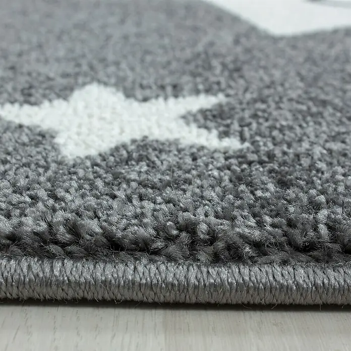 Kinderteppich Kids 0610 - Grau, Durchmesser: 160 cm, 100% Polypropylen - Nahaufnahme eines grauen Teppichs mit weißen Sternen und gekettelten Rändern, der die weiche Textur und das Design hervorhebt.