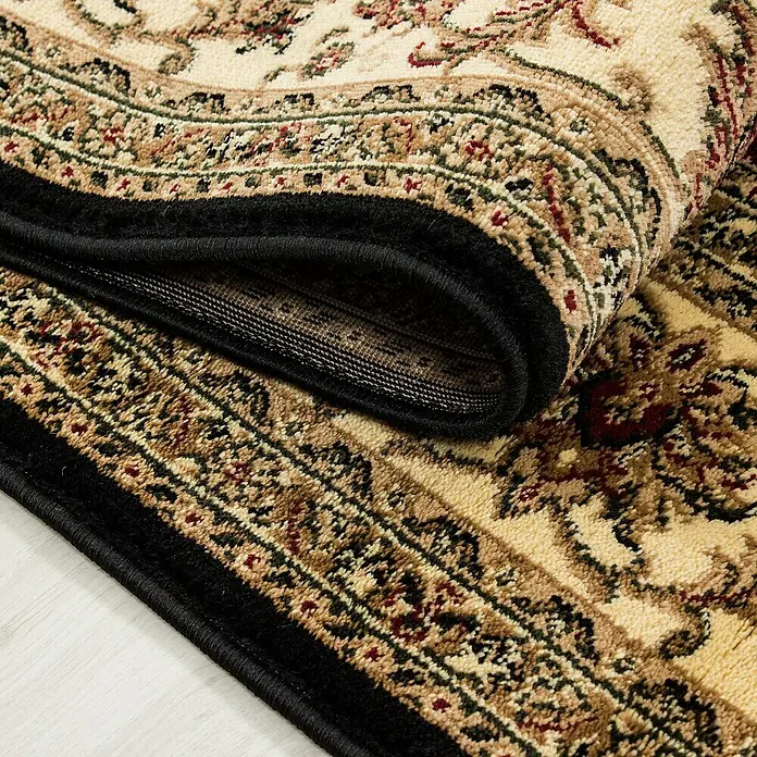 Kurzflorteppich Orient-Optik Marrakesh 0210Schwarz, 170 x 120 cm, 100% Polypropylen - Detailansicht eines orientalischen Teppichs mit beigen und braunen Mustern, gerollt, mit schwarzer Umrandung.
