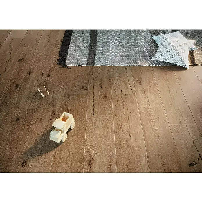Atlas Concorde Solution Fable Feinsteinzeugfliese Cognac - 22,5 x 90 cm, Dunkelbraun, Matt - Detailaufnahme eines Fußbodens mit zwei Spielzeugautos, einem Teppich und einem Kissen. Das Bild zeigt die Holzstruktur des Bodens.