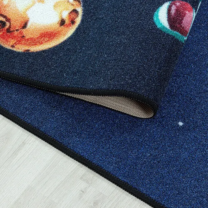 Kinderteppich Play 2910 - Navy, 150 x 100 cm, 100% Polyamide - Nahaufnahme eines Teppichs mit Planetenmuster in dunklen Blautönen und Schwarz, der auf einem hellen Holzboden liegt.