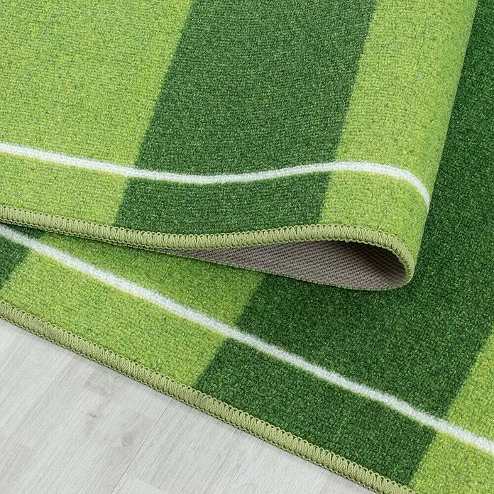 Kinderteppich Play 2911 - Grün, 120 x 80 cm, 100% Polyamide - Detailaufnahme eines grünen Teppichs mit Streifen und Rollkante. Das Produkt überzeugt durch Farbe und Textur.