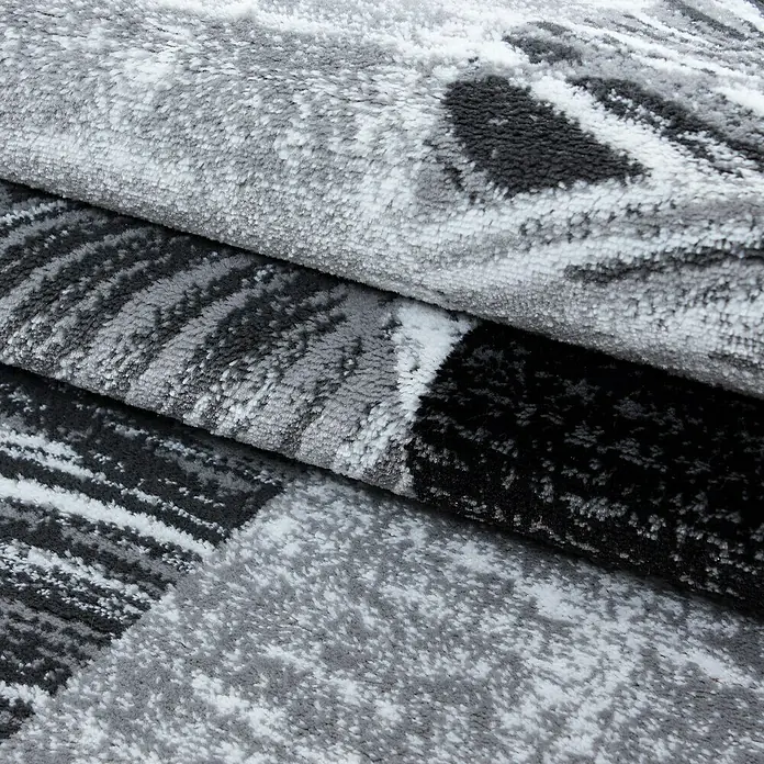 Kurzflorteppich Parma 9220Schwarz, 150 x 80 cm, 100% Polypropylen - Nahaufnahme eines grau-schwarzen Teppichs mit abstraktem Muster. Die Textur des Teppichs ist weich und lädt zum Anfassen ein.