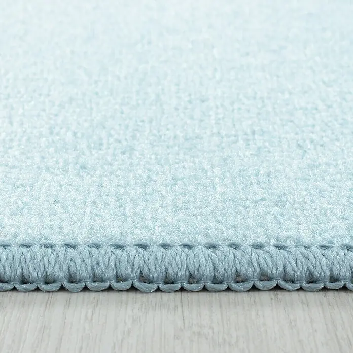 Kinderteppich Play 2908 - Blau, 230 x 160 cm, 100% Polyamide - Detailansicht eines hellblauen Teppichs mit sauberer Umrandung, der auf einem hellen Holzboden liegt. Nahaufnahme des weichen Teppichmaterials.