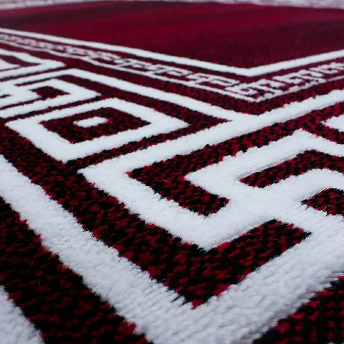 Kurzflorteppich Parma 9340Rot, 150 x 80 cm, 100% Polypropylen - Nahaufnahme eines roten Teppichs mit weißem geometrischen Muster, der ein faszinierendes Design und eine luxuriöse Textur zeigt.