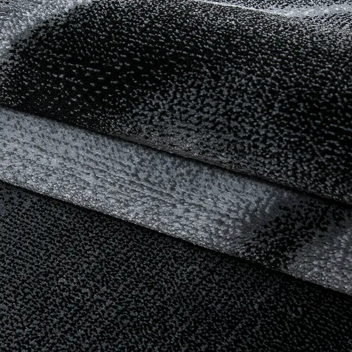 Kurzflorteppich Parma 9240Schwarz, 150 x 80 cm, 100% Polypropylen - Nahaufnahme eines grauen Teppichs mit auffälliger Textur und Farbverläufen, die eine luxuriöse und moderne Optik erzeugen.