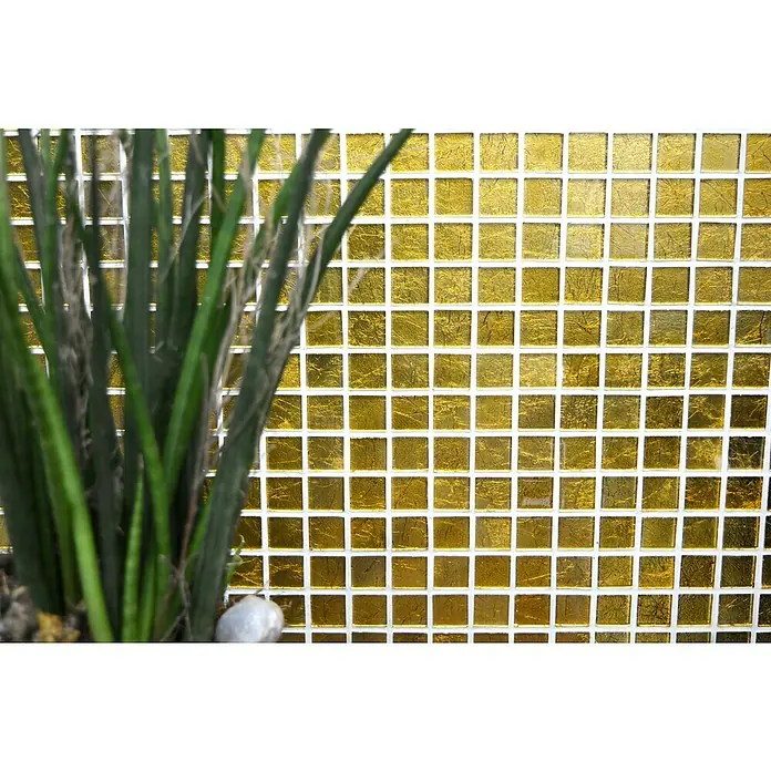 Mosaikfliese Quadrat Crystal Uni CM 4GO10 - 30 x 30 cm, Gold, Glänzend - Nahaufnahme einer goldenen Mosaikfliese mit einem subtilen Glanz, ergänzt durch die grünen Farbtöne einer Pflanze im Vordergrund.