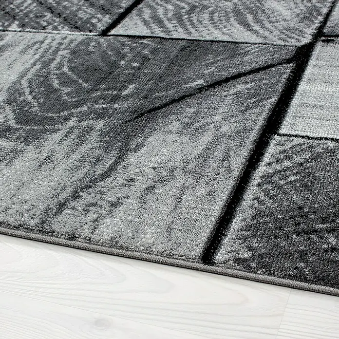 Kurzflorteppich Parma 9260Schwarz, 260 x 160 cm, 100% Polypropylen - Nahaufnahme eines grauen Teppichs mit abstraktem geometrischem Muster auf einem hellen Holzboden, der eine moderne und stilvolle Ästhetik zeigt.