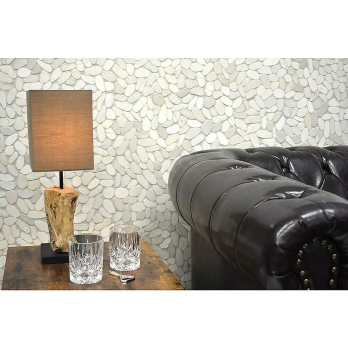 Mosaikfliese Kiesel Uni XKS IN14 - 30,5 x 30,5 cm, Weiß, Matt - Nahaufnahme von zwei Kristallgläsern und einer Lampe auf einem Holztisch neben einem schwarzen Ledersofa vor einer Steinwand.