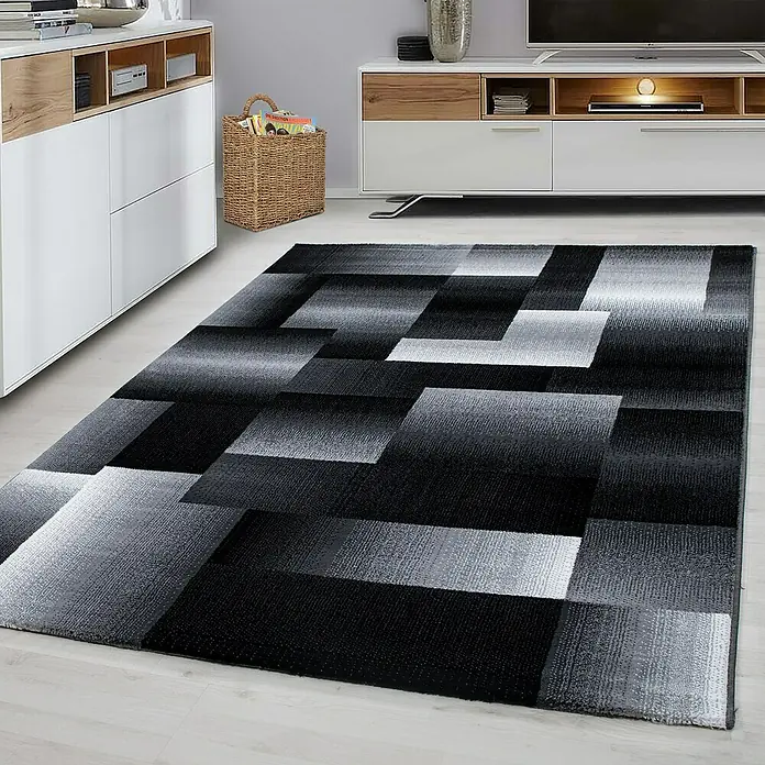 Kurzflorteppich Miami 6560 - Schwarz, 150 x 80 cm, 100% Polypropylen - Ein moderner Teppich mit einem geometrischen Muster in Schwarz-, Grau- und Weißtönen liegt in einem stilvollen Wohnzimmer.