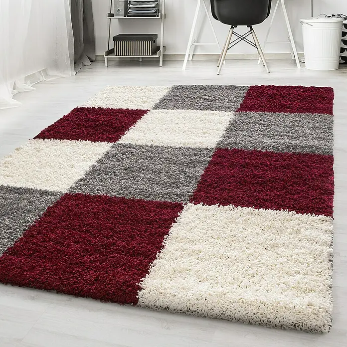 Hochflorteppich Life 1501Rot, 110 x 60 cm, 100% Polypropylen - Ein weicher, hochfloriger Teppich mit einem geometrischen Muster aus weißen, grauen und burgunderroten Quadraten liegt auf einem hellen Holzboden.