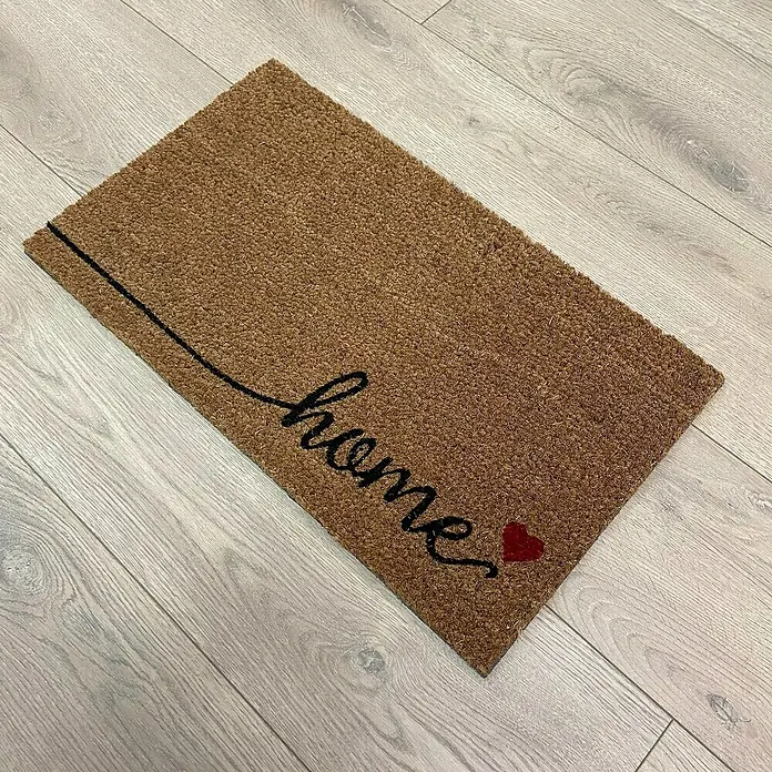 Felpudo Sweet Home - 60 x 35 cm, Negro/Natural, Home - Un felpudo marrón con la palabra "home" en letra negra y un pequeño detalle de corazón rojo, ideal para cualquier entrada.