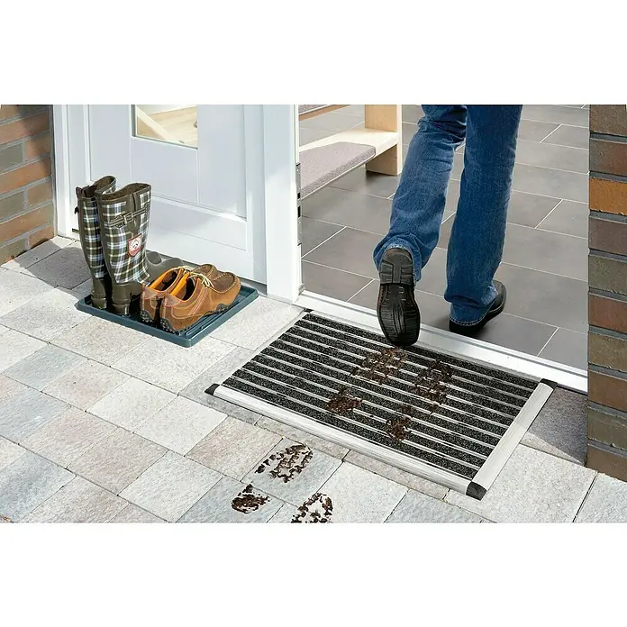 Astra Fußmatte Excellence Mat - Aluminium, Anthrazit/Grau, 40 x 60 cm - Fußmatte mit Schmutzfänger-Design vor einer Haustür mit Schuhen und Stiefeln. Der Fokus liegt auf der praktischen Sauberkeit und dem Schutz des Eingangsbereichs.