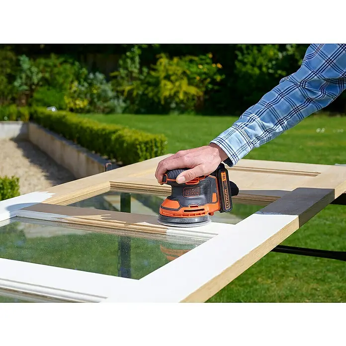 Black+Decker Akku-Exzenterschleifer BDCROS18-QW - 18 V, Li-Ionen, 1,5 Ah, 1 Akku, 125 mm - Nahaufnahme eines Akku-Exzenterschleifers von Black+Decker beim Abschleifen eines Fensterrahmens im Freien.