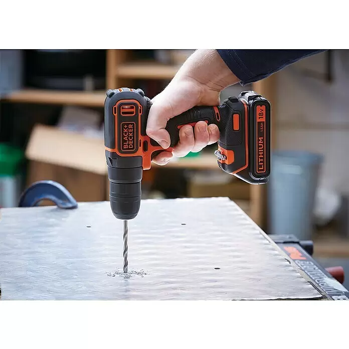 Black+Decker Taladro atornillador percutor de batería BDCHD18KB - 18 V, 2 baterías, 1,5 Ah, 40 Nm - Taladro inalámbrico Black+Decker naranja y negro, sujetado por una mano, perforando activamente una lámina metálica, creando virutas.