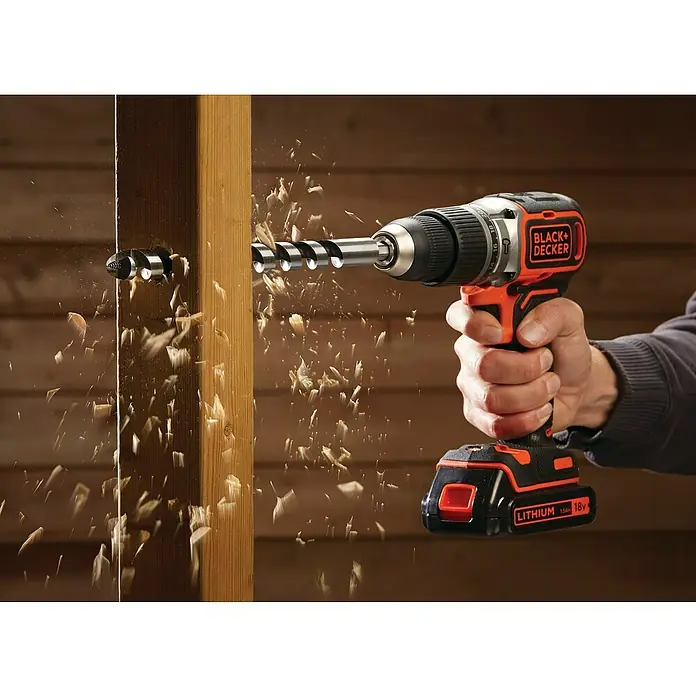 Black+Decker Akku-Schlagschrauber BL188K-QW18 V, 1 Akku, 1,5 Ah - Eine Bohrmaschine der Marke BLACK+DECKER bohrt ein Loch in ein Holzbrett, Holzspäne fliegen umher.