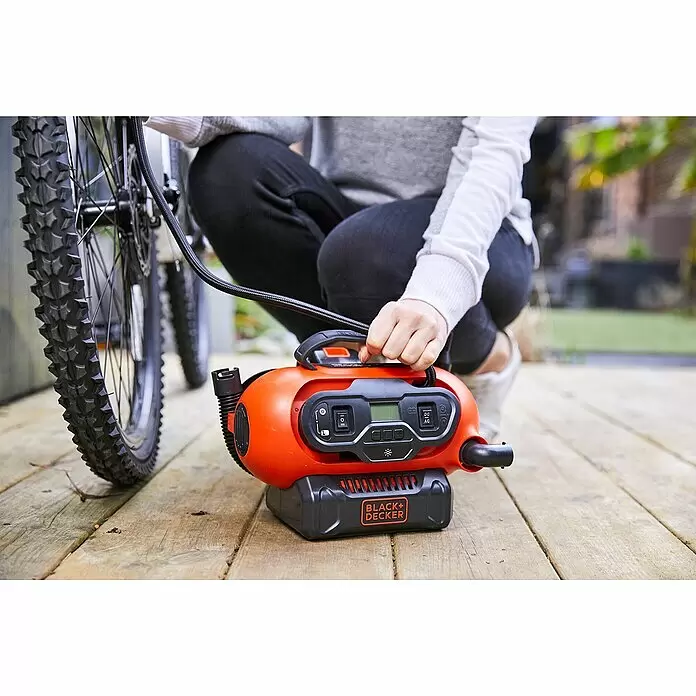 Black+Decker Akku-Kompressor BDCINF18N-QS - 18 V, Ohne Akku, 11 bar - Ein orange-schwarzer BLACK+DECKER Kompressor pumpt einen Fahrradreifen auf, gehalten von einer Person auf Holzterrasse.
