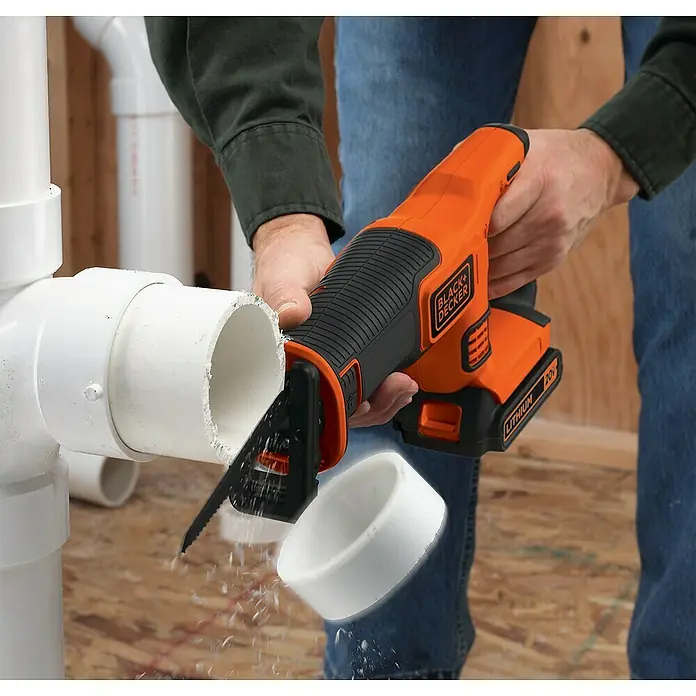Black+Decker Akku-Säbelsäge BDCR18-QW - 18 V, 1 Akku, 1,5 Ah, 0 /min - 3.000 /min - Eine Black+Decker Akku-Säbelsäge schneidet ein PVC-Rohr, Späne fliegen. Das Werkzeug ist orange-schwarz mit 20V Lithium-Akku.