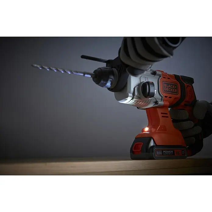 Black+Decker Akku-Kombihammer BCD900E2K-QW - 18 V, 2 Akkus, 1,2 J - Akkubetriebener Black+Decker-Bohrhammer mit LED-Licht und Bohraufsatz, der auf einer Holzoberfläche steht und von behandschuhten Händen gehalten wird.