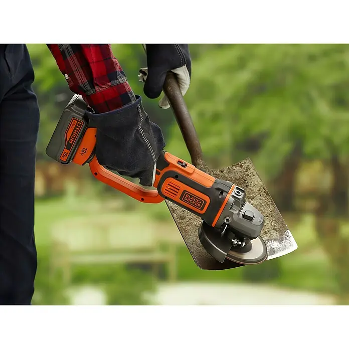 Black+Decker Akku-Winkelschleifer BCG720M1-QW - Li-Ionen, 4 Ah, 1 Akku, Durchmesser Scheibe: 125 mm, 8.600 U/min - Nahaufnahme eines Black+Decker Akku-Winkelschleifers, der eine Schaufel schärft. Der Winkelschleifer ist orange und schwarz.