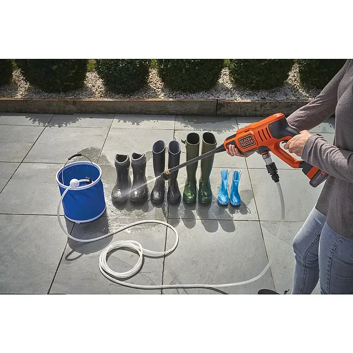 Black+Decker Akku-Druckreiniger BCPC18B - 18 V, Ohne Akku, 120 l/h - Eine Person reinigt Gummistiefel mit einem tragbaren, orangefarbenen BLACK+DECKER-Hochdruckreiniger und einem blauen Eimer.
