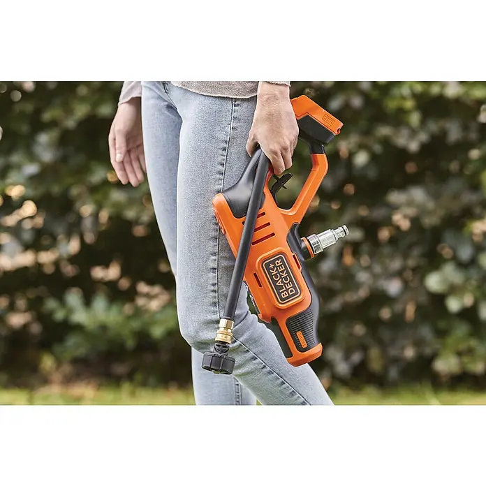 Black+Decker Akku-Druckreiniger BCPC18B - 18 V, Ohne Akku, 120 l/h - Eine Person hält einen Black+Decker-Reiniger in Orange und Schwarz vor einem grünen Hintergrund.