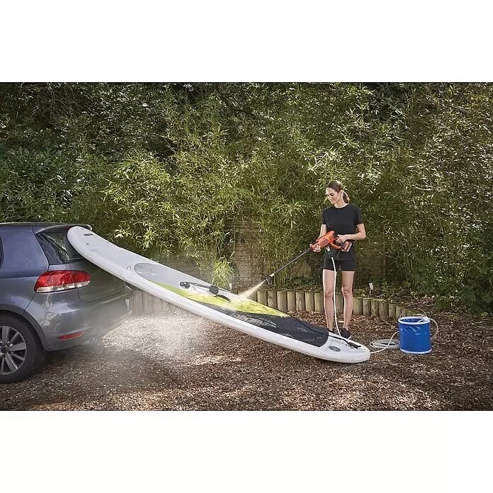 Black+Decker Akku-Druckreiniger BCPC18B - 18 V, Ohne Akku, 120 l/h - Frau reinigt ein weißes Paddleboard mit einem orange-schwarzen tragbaren Hochdruckreiniger.