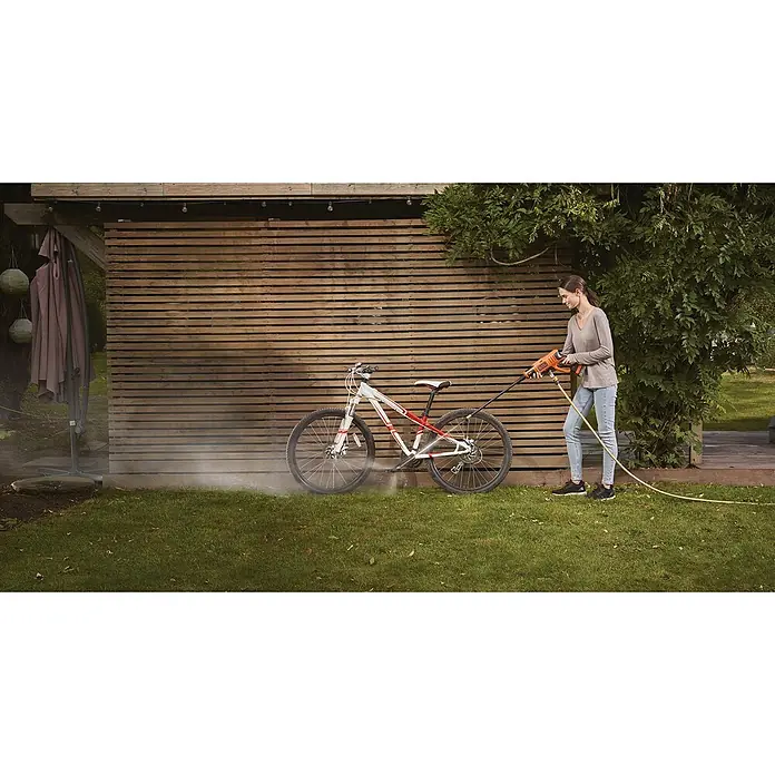 Black+Decker Akku-Druckreiniger BCPC18B - 18 V, 1 Akku, 2 Ah, 120 l/h - Frau reinigt ein Fahrrad mit einem BLACK+DECKER Hochdruckreiniger vor einer Holzwand.