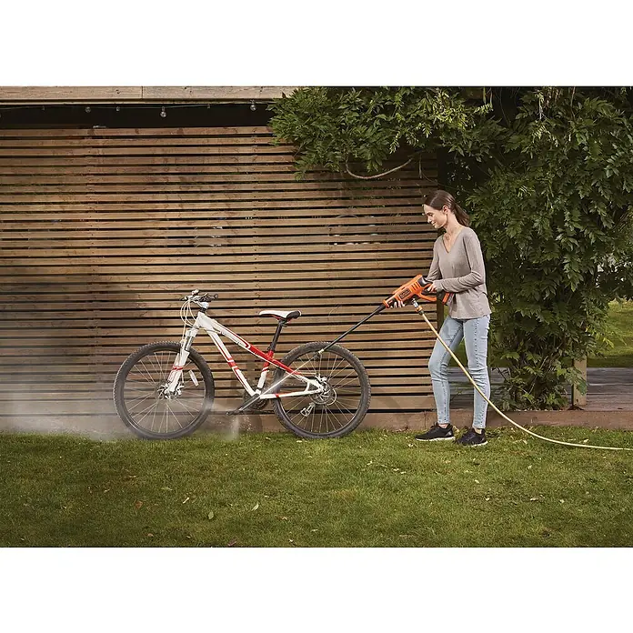 Black+Decker Akku-Druckreiniger BCPC18B - 18 V, Ohne Akku, 120 l/h - Eine Frau reinigt mit einem BLACK+DECKER Akku-Hochdruckreiniger ein Fahrrad auf einem Rasen vor einer hölzernen Wand.