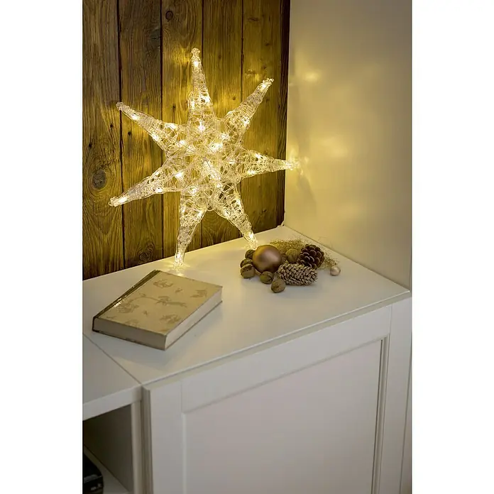 Konstsmide LED-Stern - 45 cm, Farblos, Lichtfarbe: Warmweiß, IP20, Netzbetrieben - Stimmungsvolle Dekoration mit einem leuchtenden Stern, Buch und winterlichen Elementen auf einem weißen Schrank.