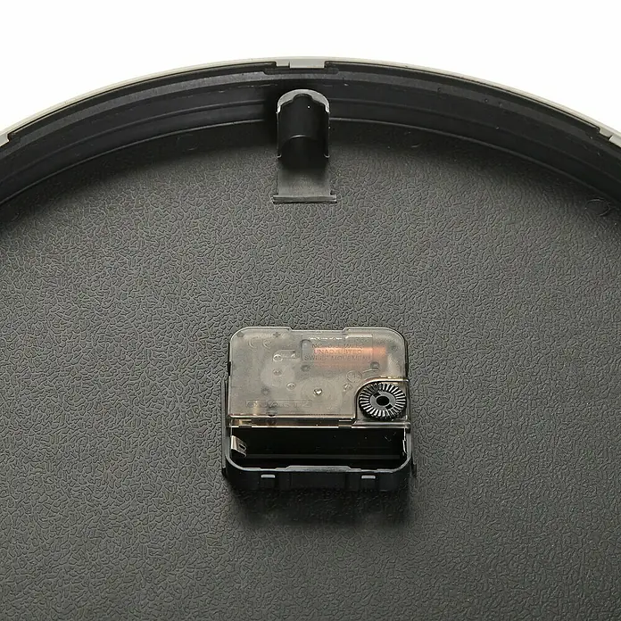 Versa Reloj de pared Cocina - Diámetro: 30,5 cm, Negro - Primer plano del mecanismo de un reloj de pared que muestra el funcionamiento interno y el compartimento de la batería.