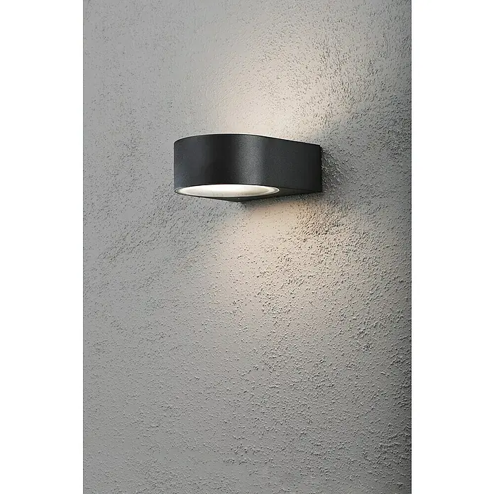Konstsmide Außenwandleuchte - 40 W, 18,5 x 17 x 7 cm, Schwarz, IP44 - Wandleuchte aus dunklem Metall an einer grauen Wand, die ein warmes Licht ausstrahlt. Moderne Beleuchtung für Innen- und Außenbereiche.