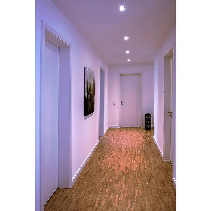 Müller-Licht Tint LED-Einbauleuchten-Set - 19 W, Weiß, 3 Stk., RGBW - Flur mit Holzboden, weißen Wänden, Türen und Deckenleuchten. Das Bild zeigt einen modernen und minimalistischen Einrichtungsstil.